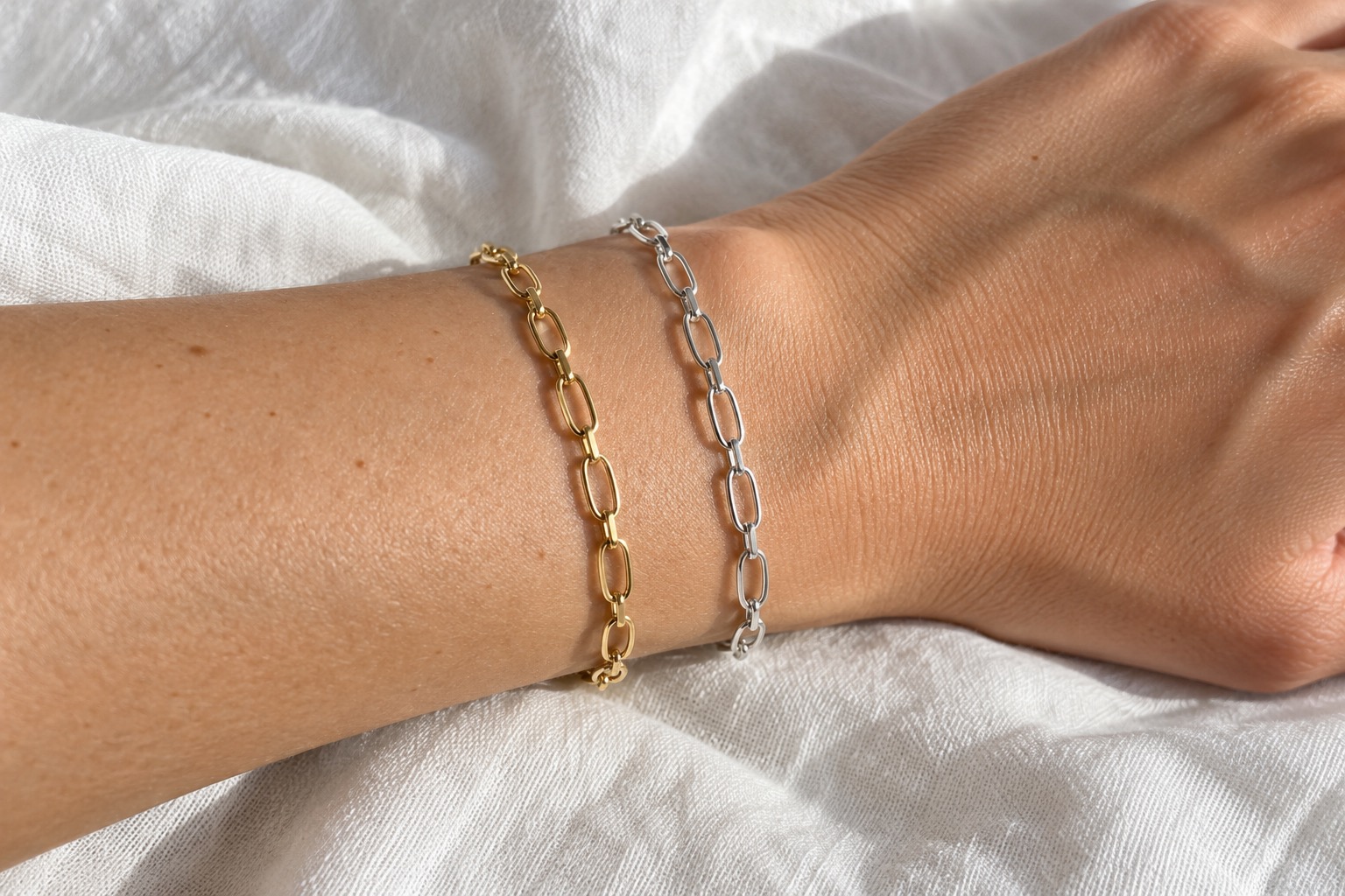 Yellow gold and sterling silver chains on a wrist over white linen in natural window light