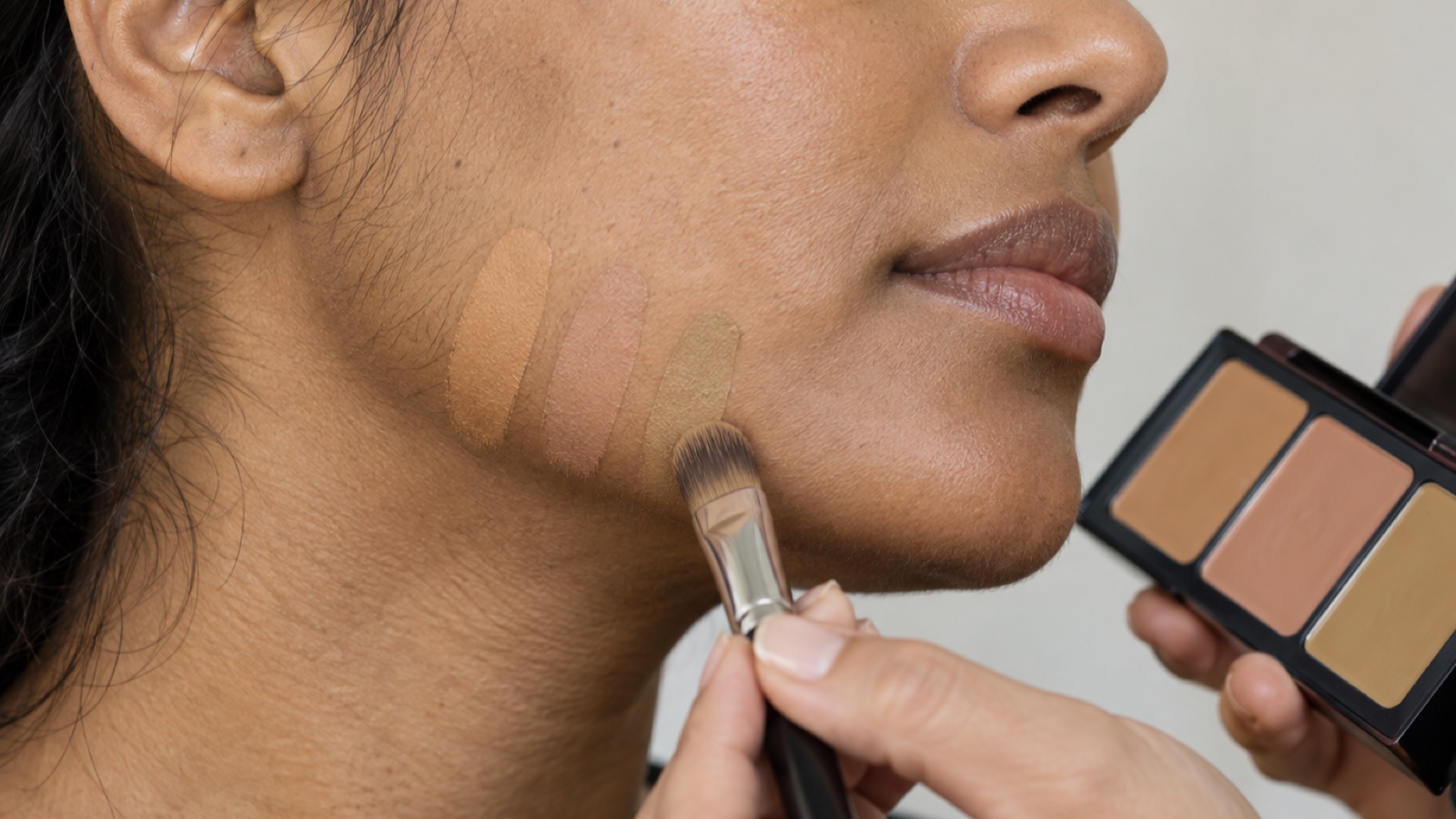 Three equal-depth peach rosy-neutral and muted olive-neutral foundation swatches applied along a woman's jaw in daylight